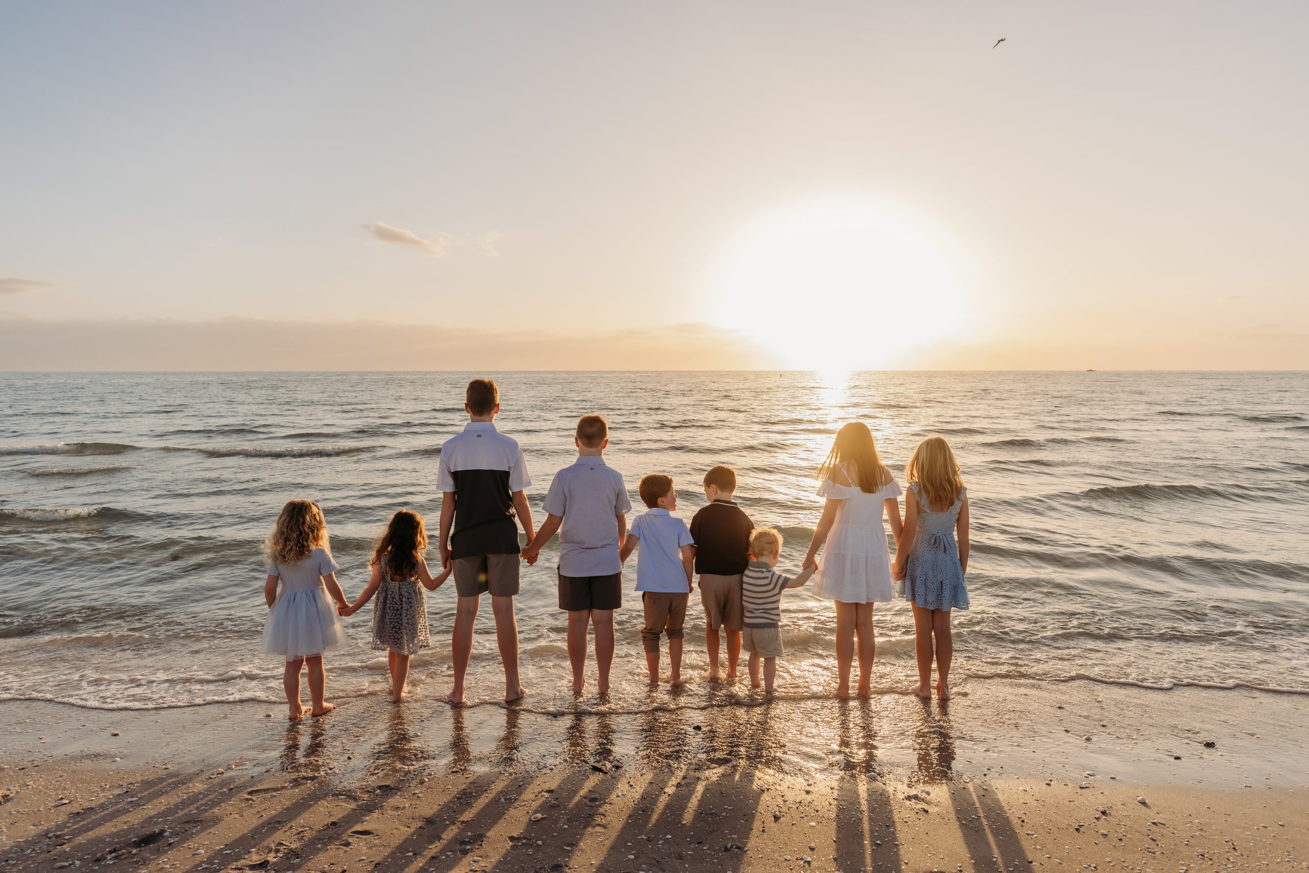 Nine cousins holding hands at the water edge, watching the sun set over the Gulf of Mexico in Naples, Florida