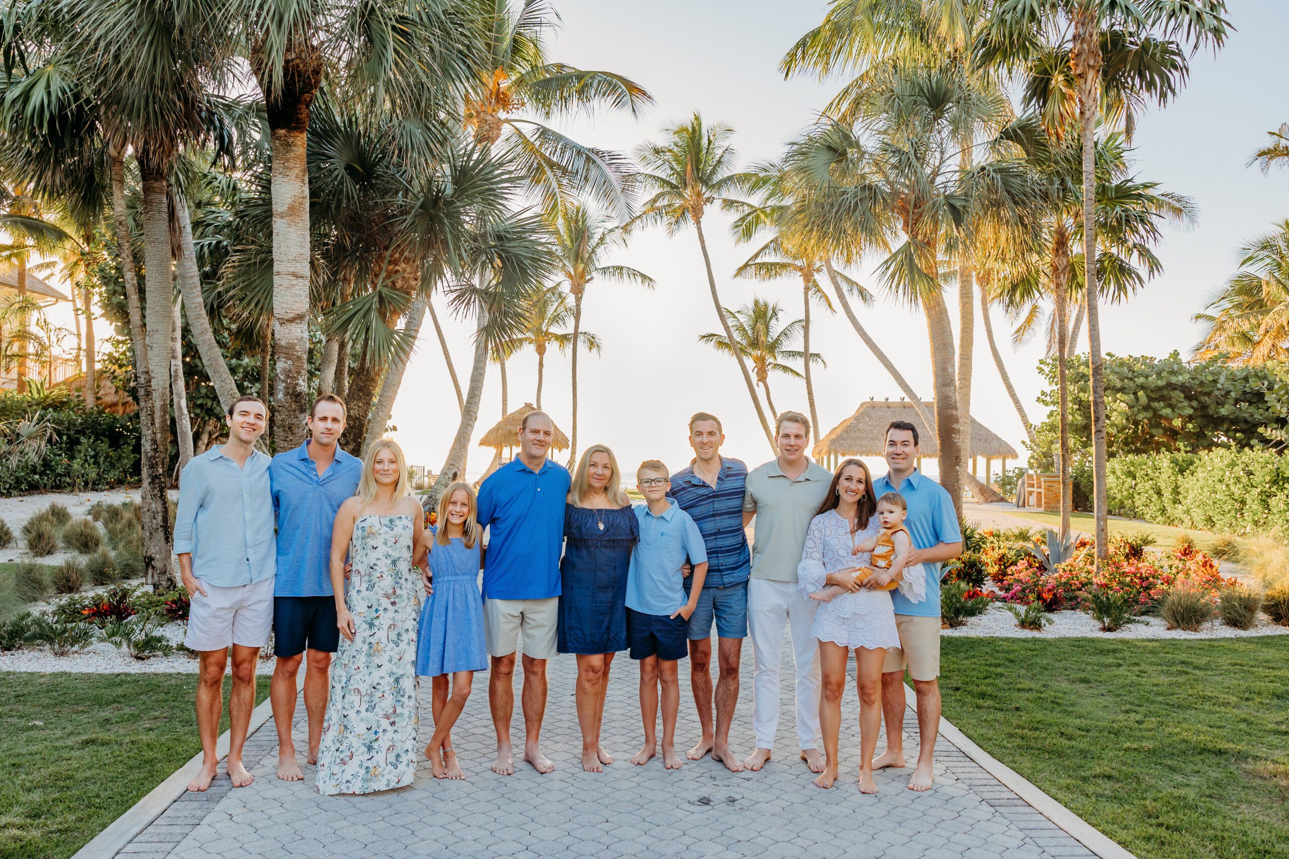 An extended family of thirteen in coordinated blues on a palm lined path in Naples, three generations together before sunset