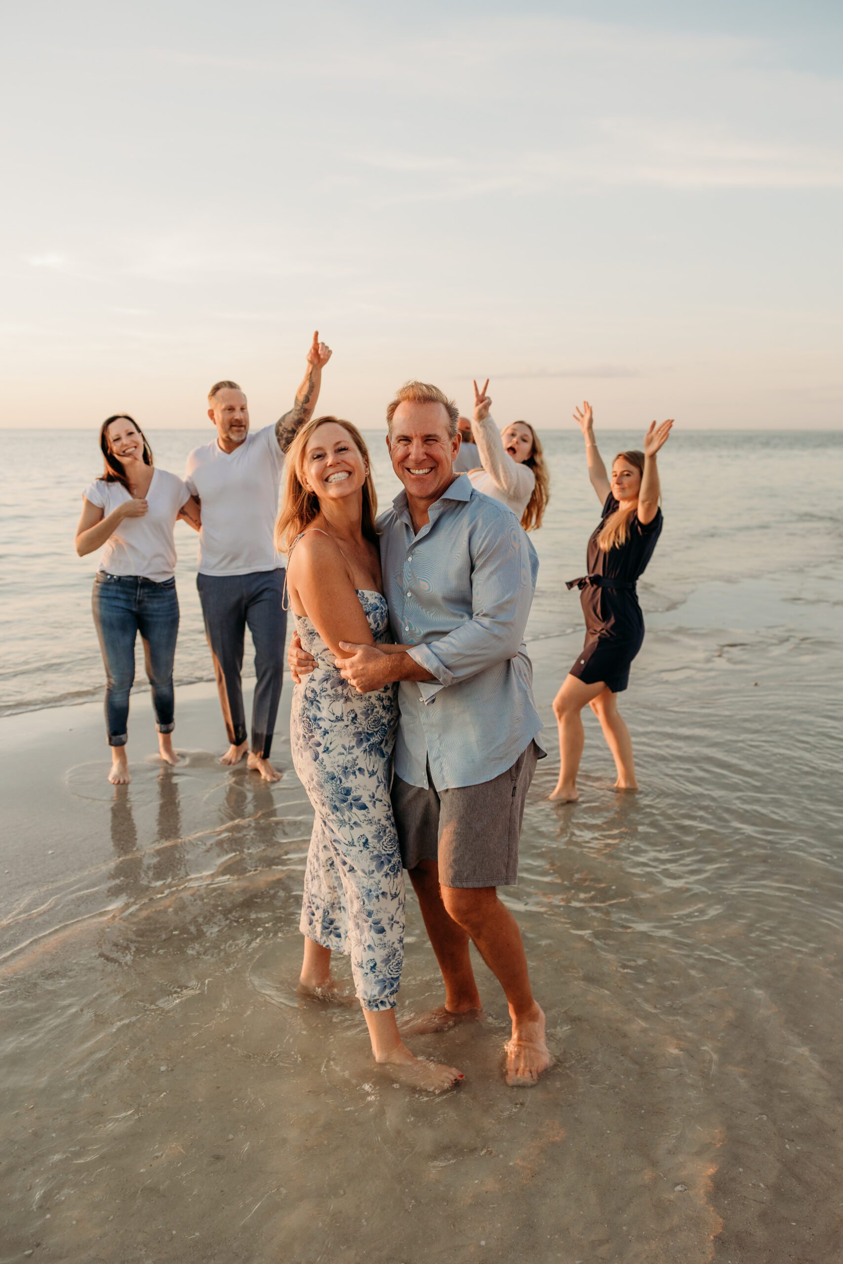 A couple laughing together in the shallow water at sunset in Naples while the rest of their extended family celebrates behind them